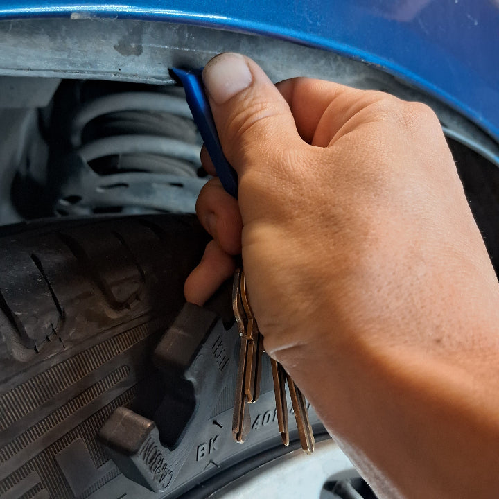 A car fender liner being moved out of the way with a pry tool to gain access for PDR